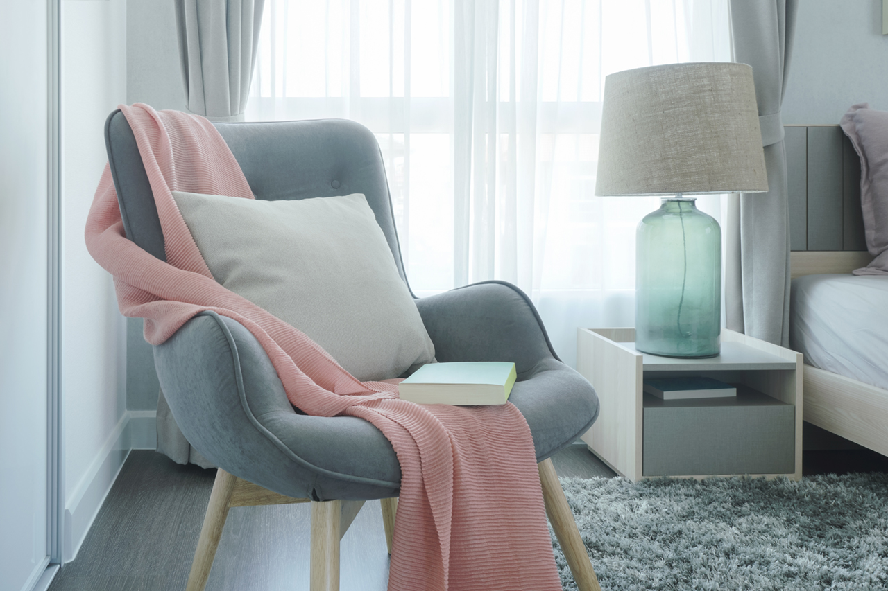 Gray-easy-armchair-with-pink-scarf,-pillow-and-book-next-to-bed-in-the-bedroom